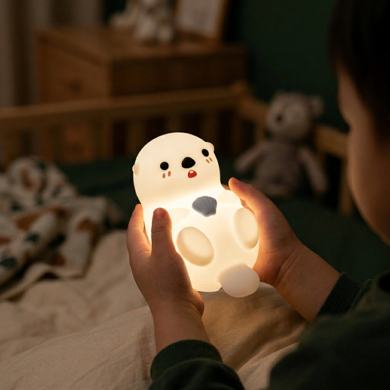 Enfant tenant une veilleuse loutre silicone allumee dans chambre obscure lumiere douce apaisante — Tendre Veilleuse
