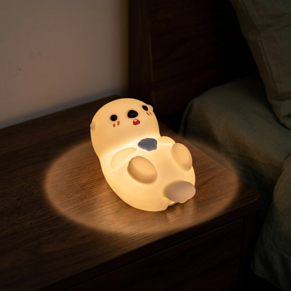 Veilleuse loutre silicone allumee posee sur table de nuit dans chambre enfant obscure halo lumineux doux — Tendre Veilleuse
