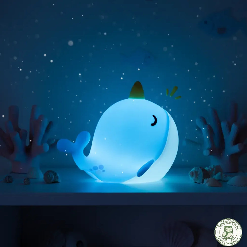 Veilleuse narval allumée la nuit diffusant une lumière bleue douce dans une chambre d'enfant au décor sous-marin étoilé