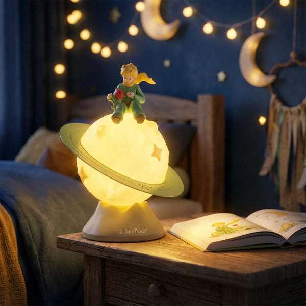 La Veilleuse Petit Prince allumée diffuse une lumière chaude apaisante sur une table de chevet la nuit, accompagnée de guirlandes lumineuses pour le rituel du coucher.