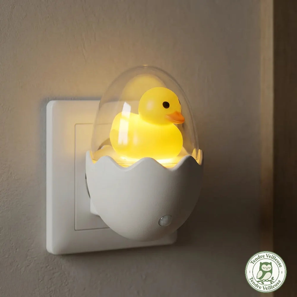 Gros plan sur la veilleuse prise secteur LED en forme de canard dans sa coquille sécurisée qui ne chauffe pas et diffuse une lumière jaune sommeil économique pour rassurer bébé sans perturber sa mélatonine.