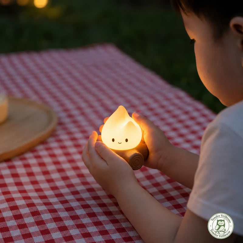 Gros plan sur les mains d'un enfant touchant la flamme en silicone de la veilleuse, démontrant la matière souple et la sécurité de la LED qui ne chauffe pas.