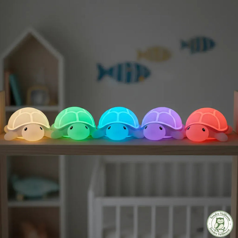 Alignement de veilleuses tortue en silicone illustrant les différentes couleurs d'éclairage LED disponibles : blanc chaud, vert, bleu, violet et rouge, pour adapter l'ambiance lumineuse de la chambre.