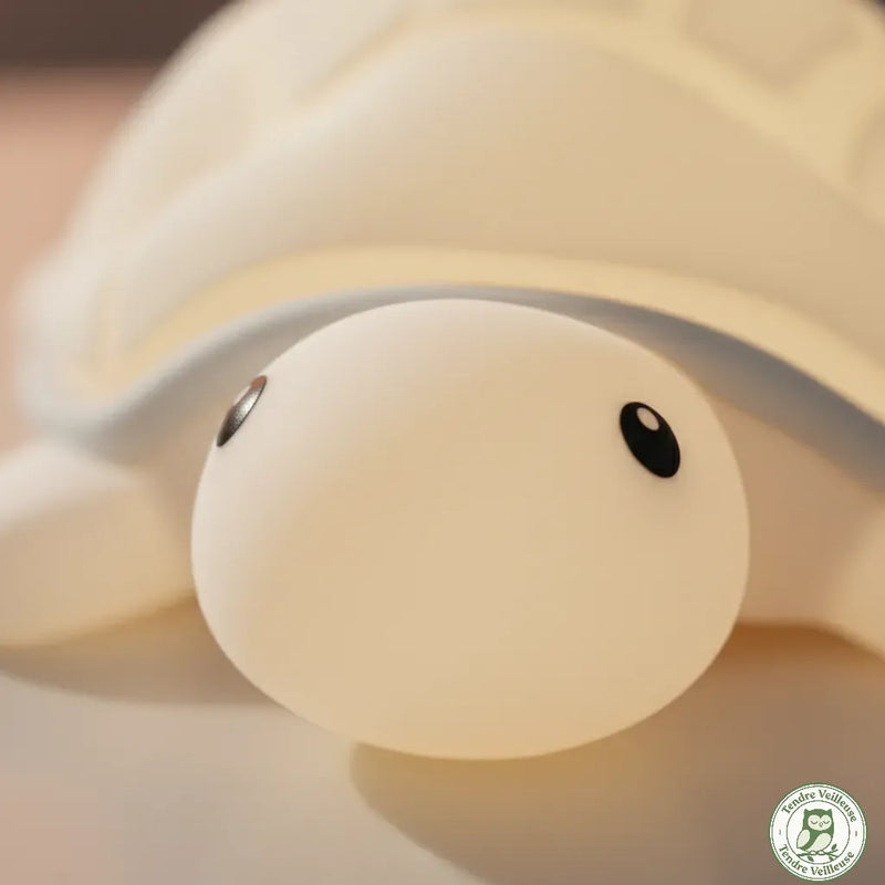 Gros plan sur le visage de la veilleuse tortue en silicone Soft Touch, illustrant sa texture douce, souple et sans arêtes vives, parfaitement sécurisée pour les petites mains de bébé.