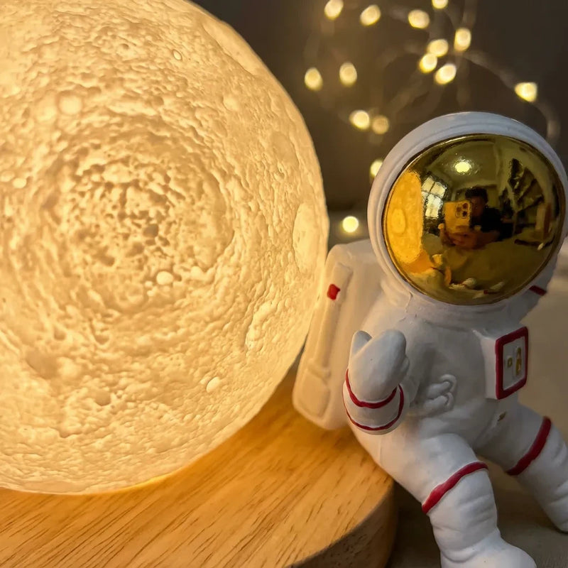 Gros plan macro sur la texture en relief du globe lunaire et le reflet dans le casque doré de la veilleuse astronaute, posée sur son socle en bois.
